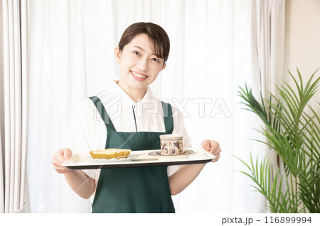 笑顔でコーヒーとケーキを運ぶカフェの女性スタッフ 116899994