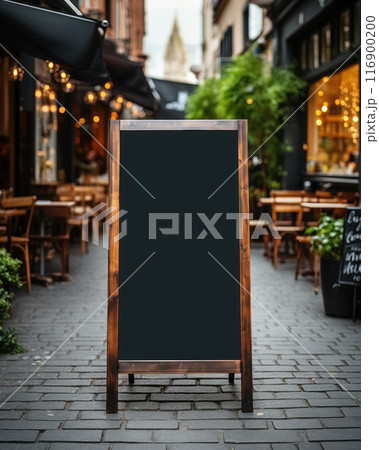 Black, empty blackboard near outdoor cozy cafes on paved street of town on blurry background. Mock up sign for menu, text or information 116900200