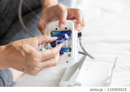 血圧計の電池を交換している男性の手元 116900828