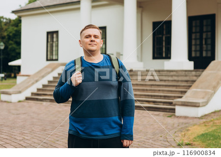 Blonde man with backpack standing with serious expression on the street, old town background 116900834