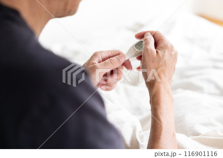 ベッドの上で体温計を触っている男性 116901116