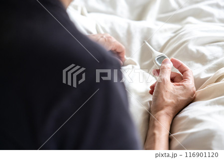 ベッドの上で体温計を触っている男性 116901120