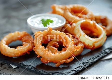 Close up of fried crispy onion rings with white sauce on cutting board on grey concrete background, delicious appetizer for beer 116901215