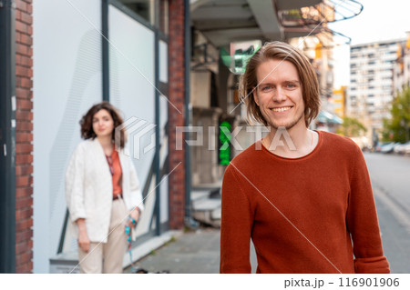 Blurred young Caucasian woman looks at handsome young man smiling looking at camera and passing by on street. Psychology of relationship Blurred young Caucasian woman looks at handsome young man smiling looking at camera and passing by on street. Psychology of relationship 116901906