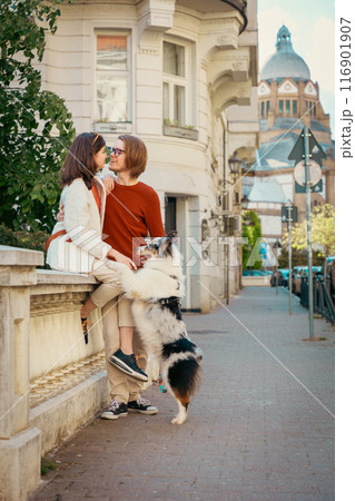 Flirting couple sitting on curb with their Aussie dog. Pet raining and city walking. Vertical 116901907