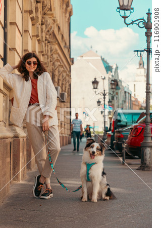 Young beautiful Caucasian woman poses outside with her purebred dog Aussie on a leash. Friendship and pet training 116901908