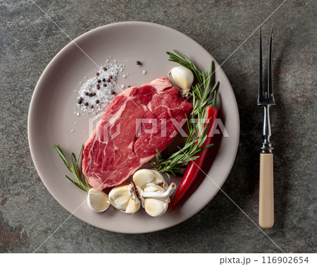Raw beef steak with rosemary, garlic, salt, and pepper. 116902654