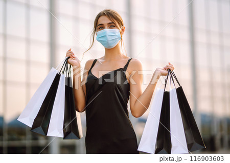 Beautiful woman in protective sterile medical mask with shopping bags near shopping center.Covid- 2019. Beautiful woman in protective sterile medical mask with shopping bags near shopping center.Covid- 2019. 116903603