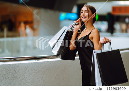 Elegant brunette woman in black dress enjoying shopping in the mall. Spring Style. Consumerism. Elegant brunette woman in black dress enjoying shopping in the mall. Spring Style. Consumerism. 116903609