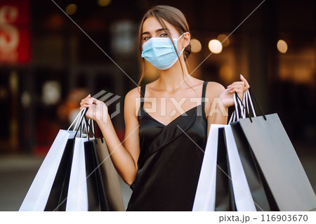 Fashionable woman in protective medical mask with shopping bags walking near mall. Covid-19. Fashionable woman in protective medical mask with shopping bags walking near mall. Covid-19. 116903670