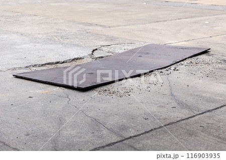 damaged concrete road surface temporary bad poor repair using thick iron sheet to cover cracked cement pavement. 116903935