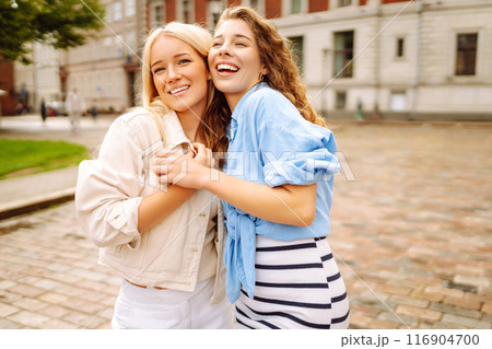 Smiling girlfriends are having fun on a sunny day on the streets of the city. Active lifestyle. 116904700