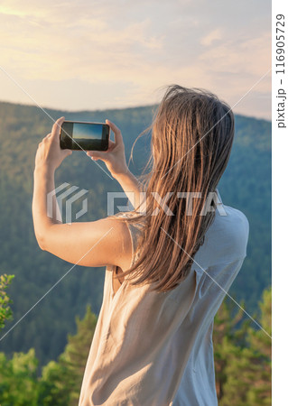 Woman captures mountain landscape on smartphone at sunset, embracing natures beauty Woman captures mountain landscape on smartphone at sunset, embracing natures beauty 116905729