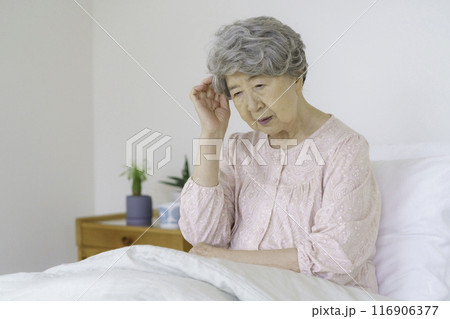 寝室で頭を抑えるシニア女性 116906377