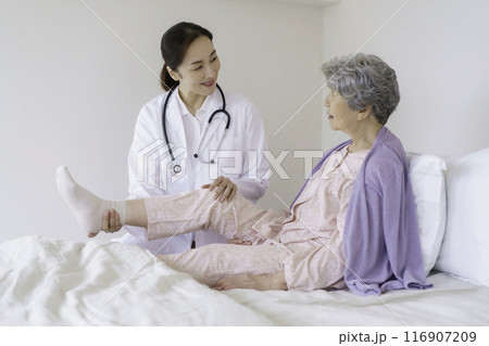 寝室で女医から膝の診察を受けるシニア女性 116907209