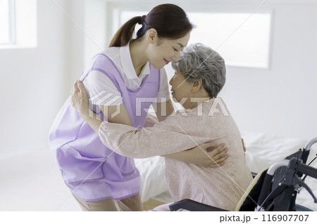 寝室でシニア女性を車椅子に座らせる看護師 116907707