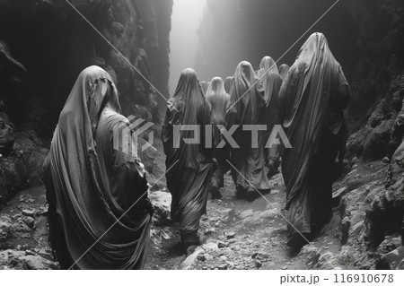 Group of pilgrims wrapped in shrouds are walking through a mountain gorge 116910678