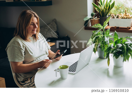 Happy 30s woman doing online shopping over laptop with credit card and phone at desk in home office. One young caucasian woman is buying online on her laptop Happy 30s woman doing online shopping over laptop with credit card and phone at desk in home office. One young caucasian woman is buying online on her laptop 116910810