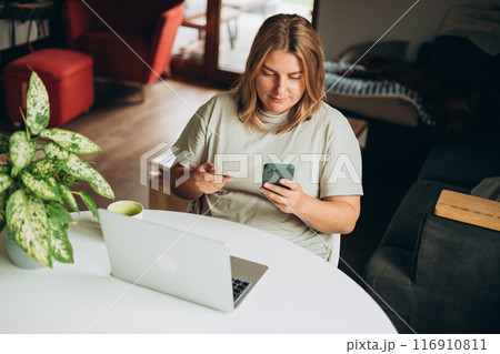 Happy 30s woman doing online shopping over laptop with credit card and phone at desk in home office. One young caucasian woman is buying online on her laptop Happy 30s woman doing online shopping over laptop with credit card and phone at desk in home office. One young caucasian woman is buying online on her laptop 116910811