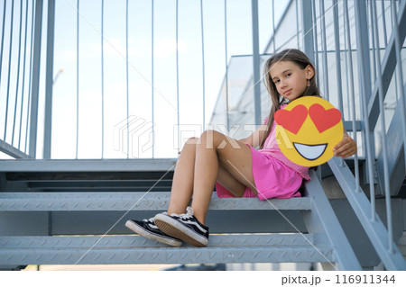 The girl demonstrates love by transmitting through emoticons. Smile face with hearts The girl demonstrates love by transmitting through emoticons. Smile face with hearts 116911344