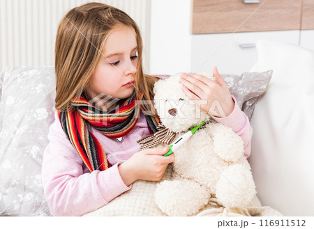 Little ill girl with scarf measuring teddy bear's temperature Little ill girl with scarf measuring teddy bear's temperature 116911512