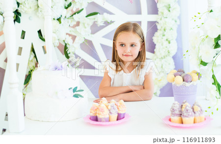 Pretty little smiling girl standing at the white table with cakes in the beatiful decorated candy bar 116911893