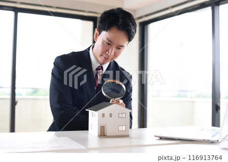 虫眼鏡で住宅模型を覗くスーツ姿の若い男性 116913764