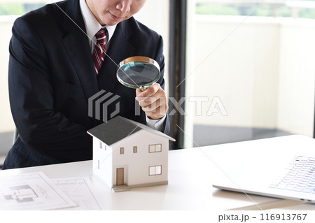 虫眼鏡で住宅模型を覗くスーツ姿の若い男性 116913767