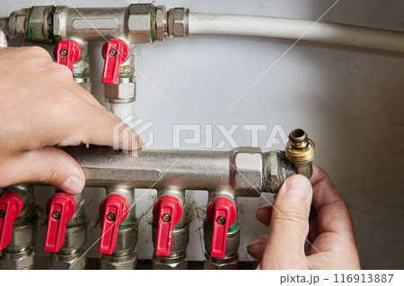 Plumber repairing water distribution collector, pipe manifold with manual control valve in home system of water supply. 116913887