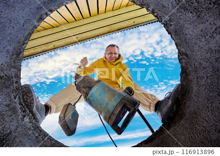 Sewer pump is immersed in wastewater through concrete ring of well, bottom view of man standing on edge of septic tank. Sewer pump is immersed in wastewater through concrete ring of well, bottom view of man standing on edge of septic tank. 116913896