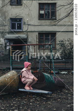 Sad little girl on a pink shabby swing in a bad neighborhood. Sad little girl on a pink shabby swing in a bad neighborhood. 116915010