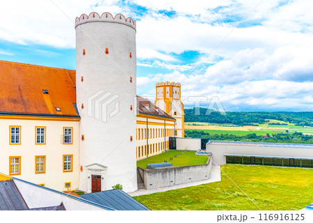 A vibrant view of Melk Abbey with its iconic yellow facade and circular tower, overlooking a scenic landscape under a partly cloudy sky. Melk, Austria 116916125