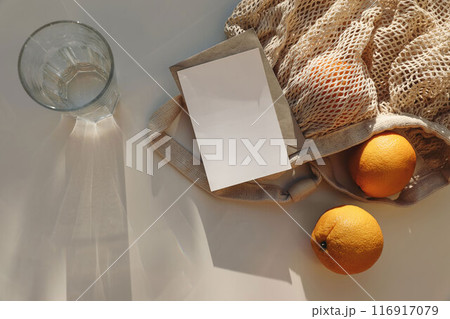Glass of water drink, string bag with oranges fruit on beige table background in sunlight. Long shadows. Summer vacation concept. Healthy fresh food, lifestyle banner. Top view, flat lay. Copy space. Glass of water drink, string bag with oranges fruit on beige table background in sunlight. Long shadows. Summer vacation concept. Healthy fresh food, lifestyle banner. Top view, flat lay. Copy space. 116917079