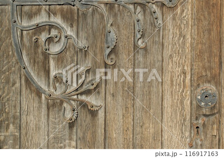 Old church door. Fragment of an antique door with a fragment of a decorative hinge. Old church door. Fragment of an antique door with a fragment of a decorative hinge. 116917163