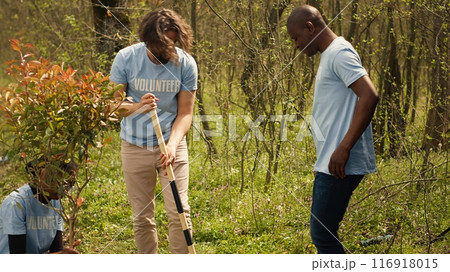 Team of climate change activists planting green trees and seeds in a forest environment, uniting to conserve ecosystem. Volunteers installing plants in the ground, nurture greenery. Camera A. Team of climate change activists planting green trees and seeds in a forest environment, uniting to conserve ecosystem. Volunteers installing plants in the ground, nurture greenery. Camera A. 116918015