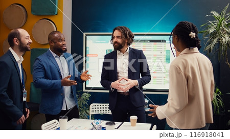 Team of startup employees gathering for a briefing session in boardroom, developing strategies to improve corporate culture and personnel engagement in multiple projects. Camera B. 116918041