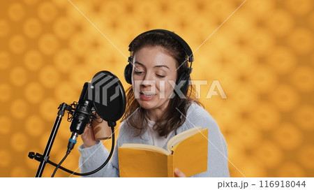 Voice actor reads book while enjoying coffee, recording audiobook using microphone, studio background. Woman using mic and headphones to produce digital recording of novel, drinking beverage, camera A 116918044