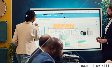 Employees team sharing insight on sales statistics in corporate briefing meeting, providing initiatives to enhance operational efficiency and agility. Group of business associates. Camera A. 116918111