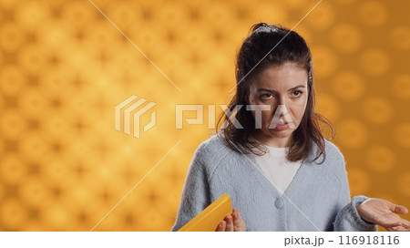 Disappointed woman bashing book, showing thumbs down hand sign, isolated over studio background. Upset bookworm dissatisfied with new novel, giving negative review, camera A 116918116