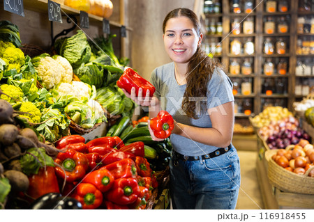 Woman picking out red bell peppers to buy in fruit and vegetables aisle of supermarket 116918455