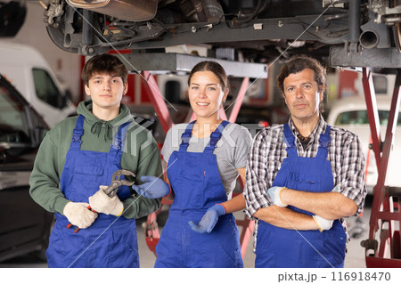 Professional team of auto repair shop posing next to hydraulic lift 116918470