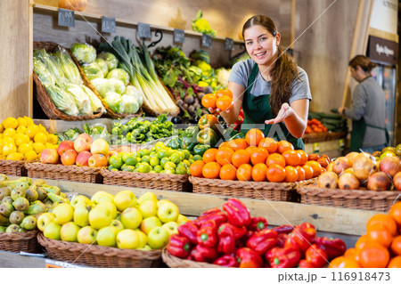 Friendly woman seller offers ripe oranges in supermarket Friendly woman seller offers ripe oranges in supermarket 116918473
