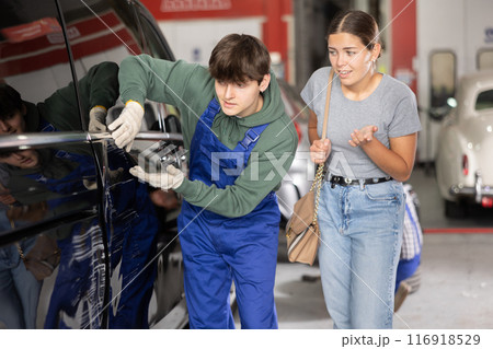 Upset girl showing dents and scratches on car door to young mechanic Upset girl showing dents and scratches on car door to young mechanic 116918529