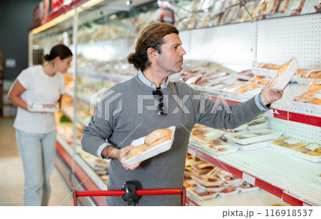 Attentive customer chooses chicken meat in the meat department of supermarket 116918537