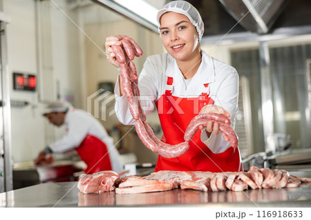 Butcher shop salesgirl offering raw pork sausages Butcher shop salesgirl offering raw pork sausages 116918633