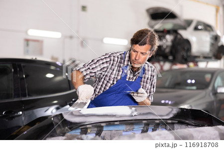 Experienced auto body technician puttying damaged car bumper 116918708