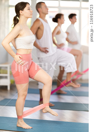 Young girl practicing hip workout with band standing on mat 116918723