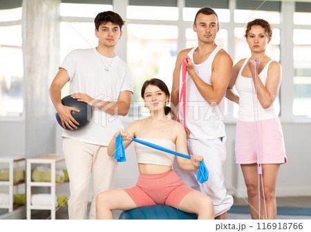 Young men and women posing together in training room holding resistance bands and pilates ball 116918766