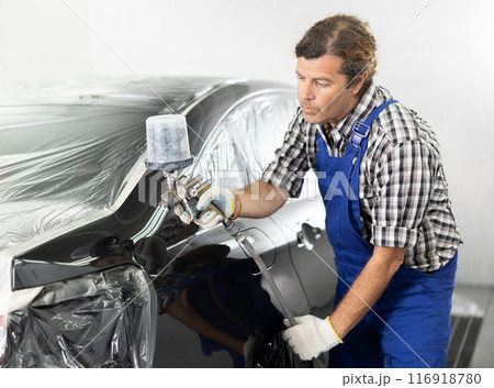 Adult male mechanic paints car with machine 116918780