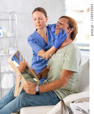 Adult female doctor examining face of male patient Adult female doctor examining face of male patient 116918803